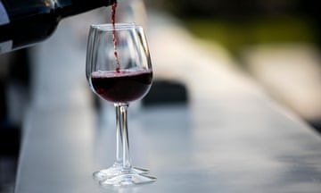 Red wine is poured into two glasses on the zinc-top counter of a bar