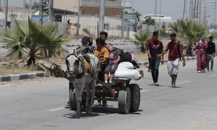 A family rides on a cart drawn by a grey donkey and heavily laden with baggage. A small boy is asleep on the cart and other people are seen walking on the highway behind.