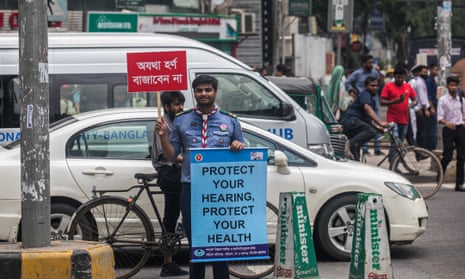 A Rover Scout holds a placard and a banner amid traffic during a No Horn campaign in Dhaka, Bangladesh.