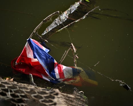 A wet Union Jack flag lies tangled in branches at the edge of murky green water