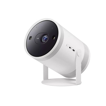A white cylindrical Samsung projector tilted upward on a round stand, with lens and vents visible