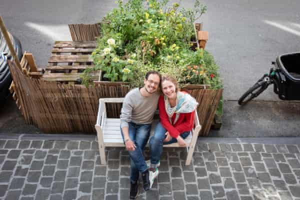 Couple are photographed from out of a window above them, sitting in front of parklet.