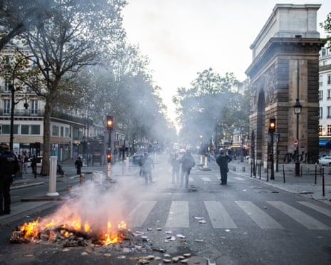 Riot police stand amid tear gas smoke near a burning pile of debris in Paris