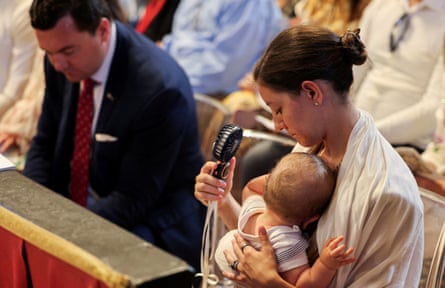 A woman holding a baby uses a handheld fan.
