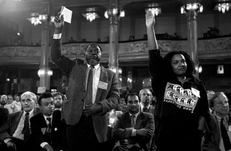 In a black and white photograph of the Labour party conference in Blackpool, MPs Bernie Grant and Diane Abbott are standing up with their hands up, watched by Paul Boateng and Keith Vaz, who are sitting behind them