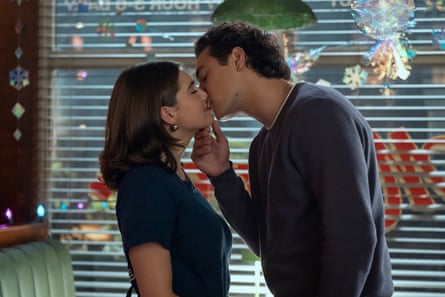 A boy and a girl kissing in front of a window with slatted blinds.