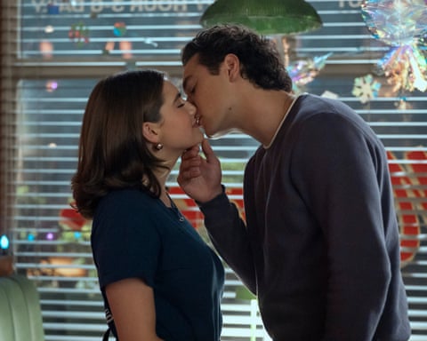 Hannah and Garrett from Off Campus kiss in front of a window with holiday decorations and lights