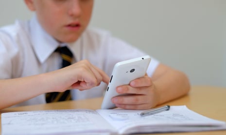 A schoolboy holding a smartphone over an open exercise book