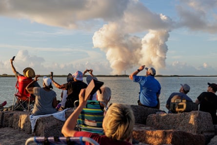 Several people looking skywards with sea, sky and smoke in background