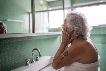 A senior-aged woman in a bathroom looking in the mirror. 