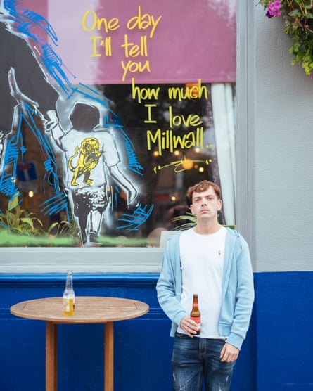 A Millwall fan with a beer bottle in front of a pub with window art that reads: ‘One day I’ll tell you how much I love Millwall’