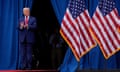 a man in a blue suit and red tie claps next to American flags