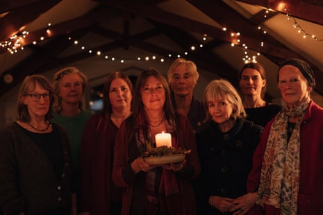 Members of a choir, with a strong of lights behind them and their leader, in centre, holding a candle