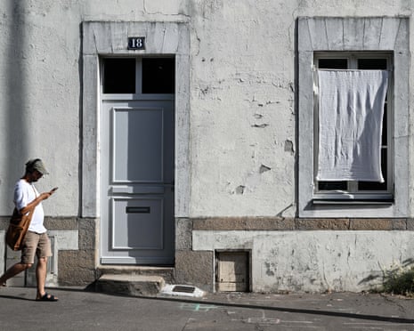 A piece of white fabric hanging over a house's window as man walks by outside