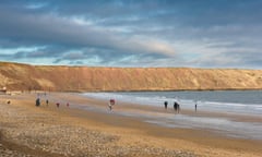 Yorkshire beach winter, view of people walking on the beach in Filey Bay with the cliffs known as Filey Brigg in the background,Yorkshire, England, UK<br>M6HRDH Yorkshire beach winter, view of people walking on the beach in Filey Bay with the cliffs known as Filey Brigg in the background,Yorkshire, England, UK