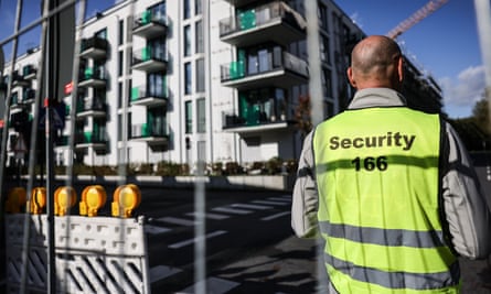 An employee of a security service stands behind a barrier in front of a residential building in the Merheim district.
