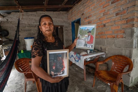 A woman wearing black holds two photographs, one of a man and another of a man holding a baby