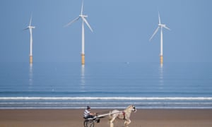 A man rides his horse and trap along the beach in front of the EDF energy windfarm at Redcar, northern England.