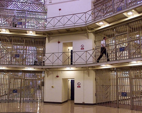 A guard walks along a walkway between tiers of Strangeways prison cells