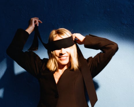 Kim Gordon, spotlit, smiling as she ties a blindfold on herself