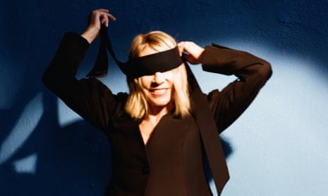 Kim Gordon, spotlit, smiling as she ties a blindfold on herself