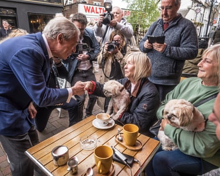 Farage shakes hands with a woman sitting at a table and holding a dog