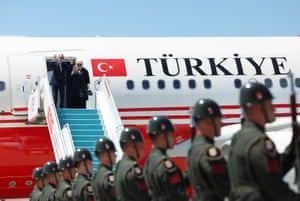 Turkey’s president, Recep Tayyip Erdoğan, and first lady Emine stand at the top of the stairs of a plane, waving with soldiers standing in a row below