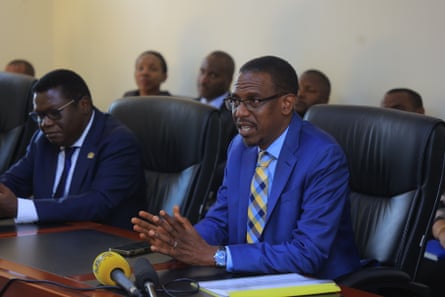 Kiryowa Kiwanuka sitting in front of a microphone in a conference room.