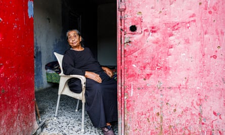 Isabel, the oldest person in the family of 20 people, sits on a chair at the door of her home.