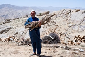 A man holds a bundle of wood in an arid mountainous landscape