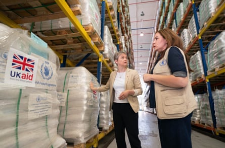 Yvette Cooper touches a wrapped sacks of supplies on a pallet in a warehouse while talking to another woman