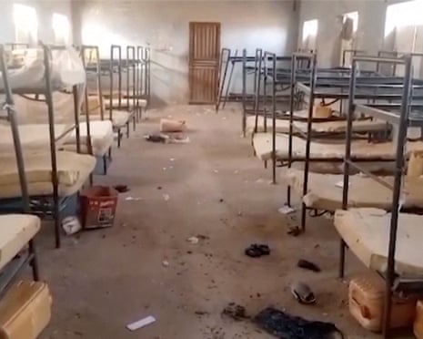 Metal beds in a bare hostel room with debris on the floor