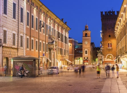 The central street of Ferrara in early evening with people out walking and only one car visible.