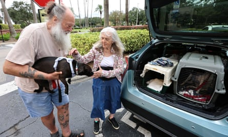 A man and woman holding their dog in front of open truck of a car