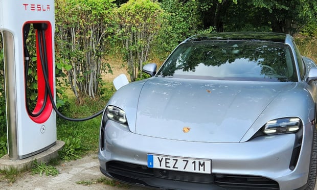 A silver Porsche EV is charged at a Tesla charging station