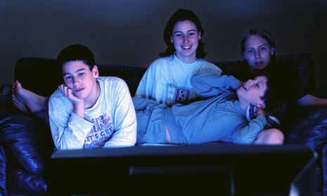 Young adults sitting together on couch watching television in the dark.