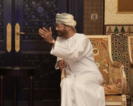 Al Busaidi in a gold-trimmed chair in a ceremonial room with carved wooden black door and panelling