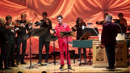 Samuel Marino wearing a red suit and singing, with musicians around him playing.