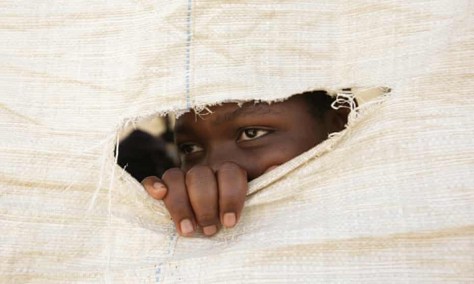 A Zimbabwean secondary school girl peeps through a hole in a sack that is used as a wall of a makeshift classroom