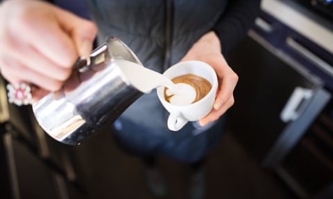 A close up of a barista pouring milk into a cup of coffee