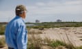 CAMERON, LOUISIANA, USA — APRIL 10TH, 2024
A man in a cap looks at a bare stretch of land with a large LNG plant in the background.