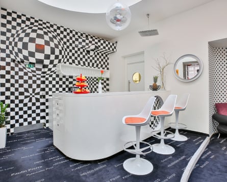 A 60s-style bar area with black-and-white check wallpaper, white plastic bar stools and orange accents
