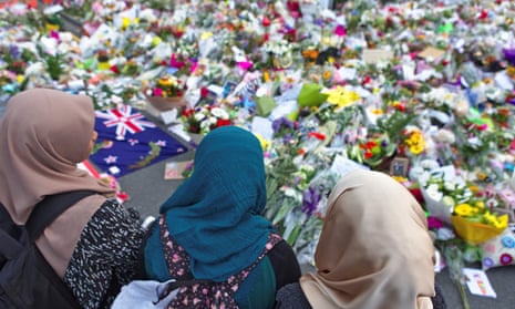 Women stand looking at piles of flowers left in tribute to the people who died in terrorist attacks in Christchurch.