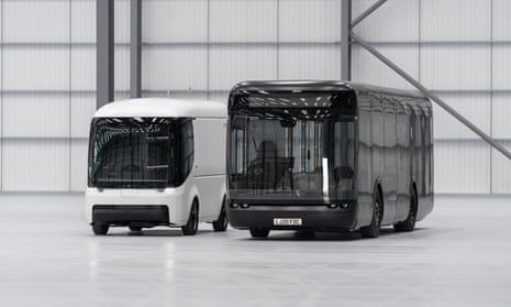 A futuristic looking bus and van, one black, the other white, in a gleaming white warehouse