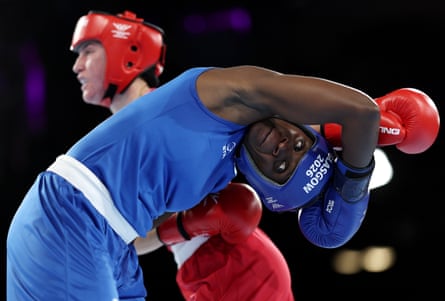 Nakalema, in blue boxing outfit, bends over to avoid a punch