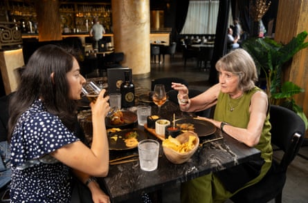Liz with her hand pointing towards Saima who is drinking red wine