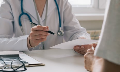 A doctor holding a pen and piece of paper sits opposite a male patient