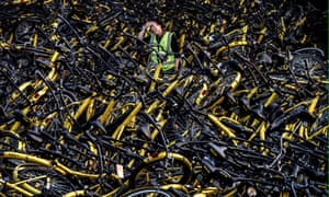 A Chinese mechanic from bike share company Ofo stands amongst a pile of thousands of damaged bicycles in need of repair.