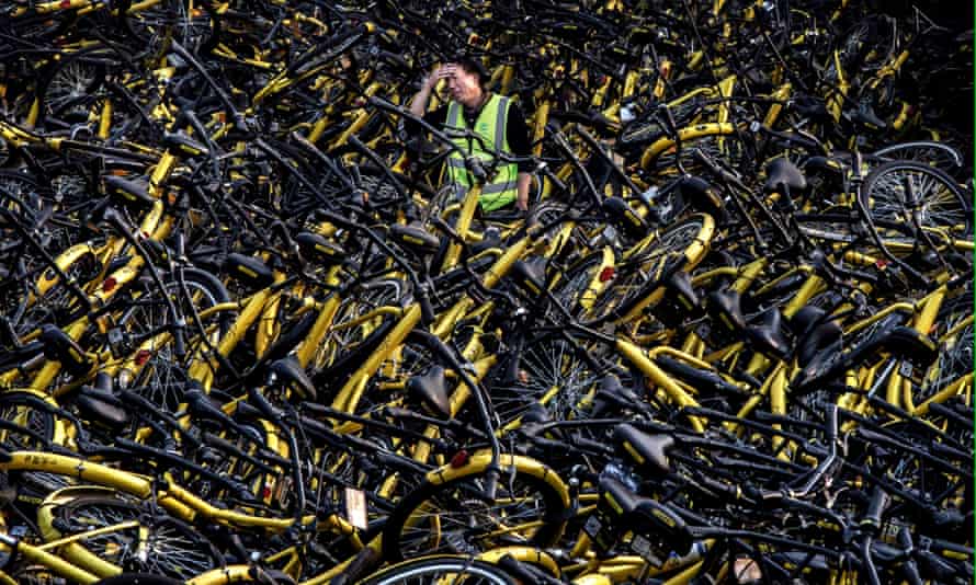 A Chinese mechanic from bike share company Ofo stands amongst a pile of thousands of damaged bicycles in need of repair.