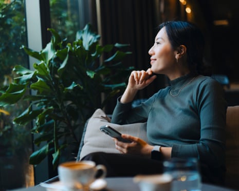 Confident young Asian woman with smartphone looking out through window